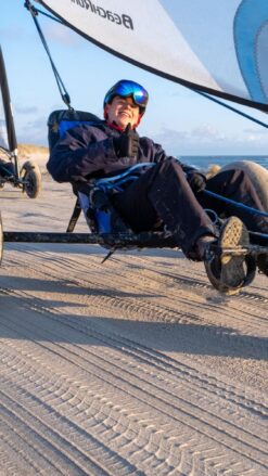 En ung mand med et stort smil på læben sidder i en strandsurfer