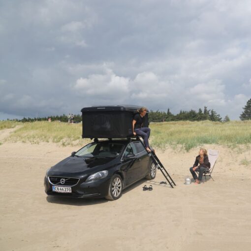 To unge kvinder på stranden med en sort bil med et tagtelt monteret