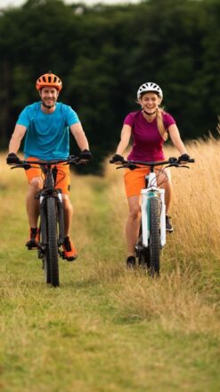 2 cyklister iført cykelhjelm på elektriske cykler på en græssti. Book en tur med Elektriske Bikes til jeres næste firmaevent. Kan arrangeres i hele landet.