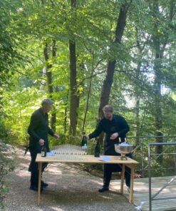 Midt på en skovsti er et bord sat op. To mænd er i gang med at hælde champagne op til gæster ved et firmaarrangement.
