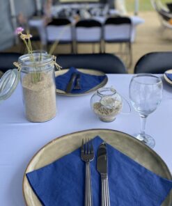 Bordopdækning til sommerfest på stranden. Blå servietter og blomster i vaser med sand.