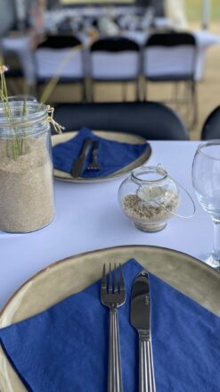 Bordopdækning til sommerfest på stranden. Blå servietter og blomster i vaser med sand.