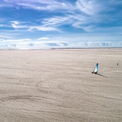 En strandsurfer fra virksomheden Ourstuff ræser hen ad en meget bred strand. Der er høj sol, blå himmel og få hvide skyer.