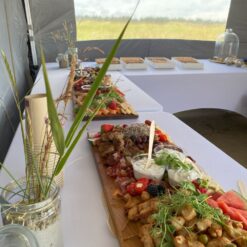 Indbydende mad arrangeret på lange træfade på hvide duge - klar til sommerfest.