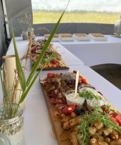 Indbydende mad arrangeret på lange træfade på hvide duge - klar til sommerfest.