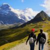 To mennesker vandrer på en grussti med et sneklædt Jungfrau bjerg i baggrunden. På firmarejse til Interlaken, Schweitz.