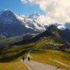 To mennesker vandrer på en grussti med et sneklædt Jungfrau bjerg i baggrunden. På firmarejse til Interlaken, Schweitz.