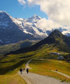 To mennesker vandrer på en grussti med et sneklædt Jungfrau bjerg i baggrunden. På firmarejse til Interlaken, Schweitz.