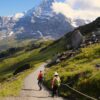 To mennesker vandrer på en grussti med et sneklædt Jungfrau bjerg i baggrunden. På firmarejse til Interlaken, Schweiz.