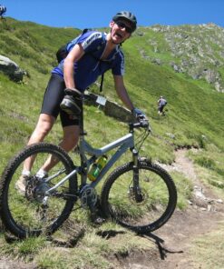 En mand står med sin mountainbike på en sti i bjergene mens solen skinner. Vi kan arrangere jeres næste firmarejse til Spanien.