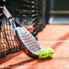 Et padel bat med to bolde står ved et net. Vi kan arrangere jeres næste firmarejse til Spanien.
