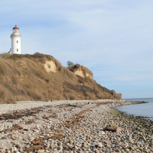 Et hvidt fyrtårn med rødt tag set fra en stenet strand på Samsø