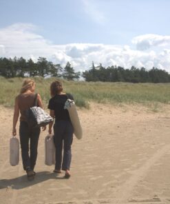 To unge kvinder går på stranden og bærer på udstyr til deres picnic.