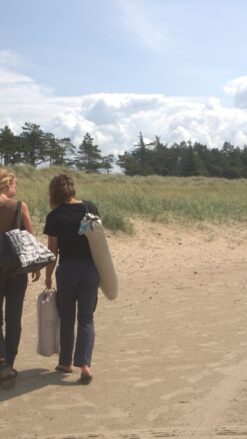 To unge kvinder går på stranden og bærer på udstyr til deres picnic.