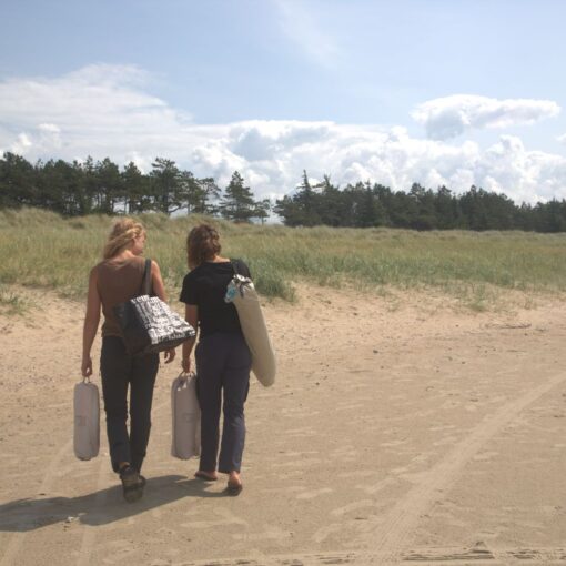 To unge kvinder går på stranden og bærer på udstyr til deres picnic.