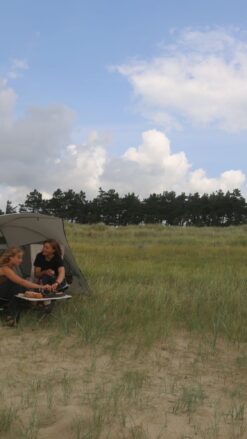 To unge kvinder nyder en picnic i det fri. De sidder i hvide stole under et læsejl.