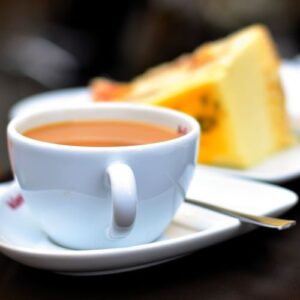 En kop kaffe med et stykke kage i baggrunden.