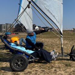 En kvindelig strandsurfer med en orange hjelm bliver vejledt af en instruktør til, hvordan man styrer en lands-/strandsurfer.