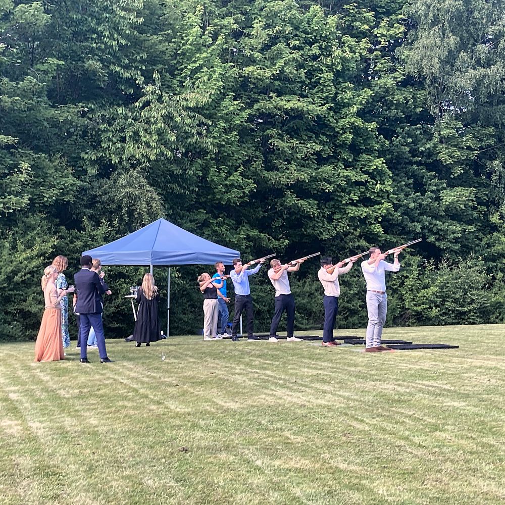 En gruppe mennesker skyder efter lerduer, mens andre kigger på. Få en sikker og sjov skydeoplevelse: ren action og sjov! Perfekt til events. Laser lerdueskydning er ideelt til teambuilding, hvor alle kan være med og bidrage til holdets succes.