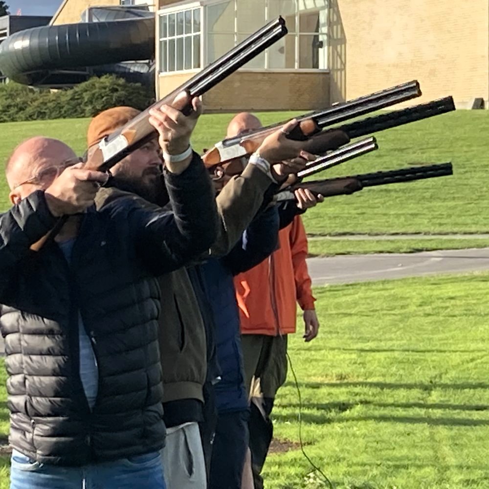 En gruppe mænd skyder efter lerduer med rifler rettet opad. Få en sikker og sjov skydeoplevelse: ren action og sjov! Perfekt til events. Laser lerdueskydning er ideelt til teambuilding, hvor alle kan være med og bidrage til holdets succes.