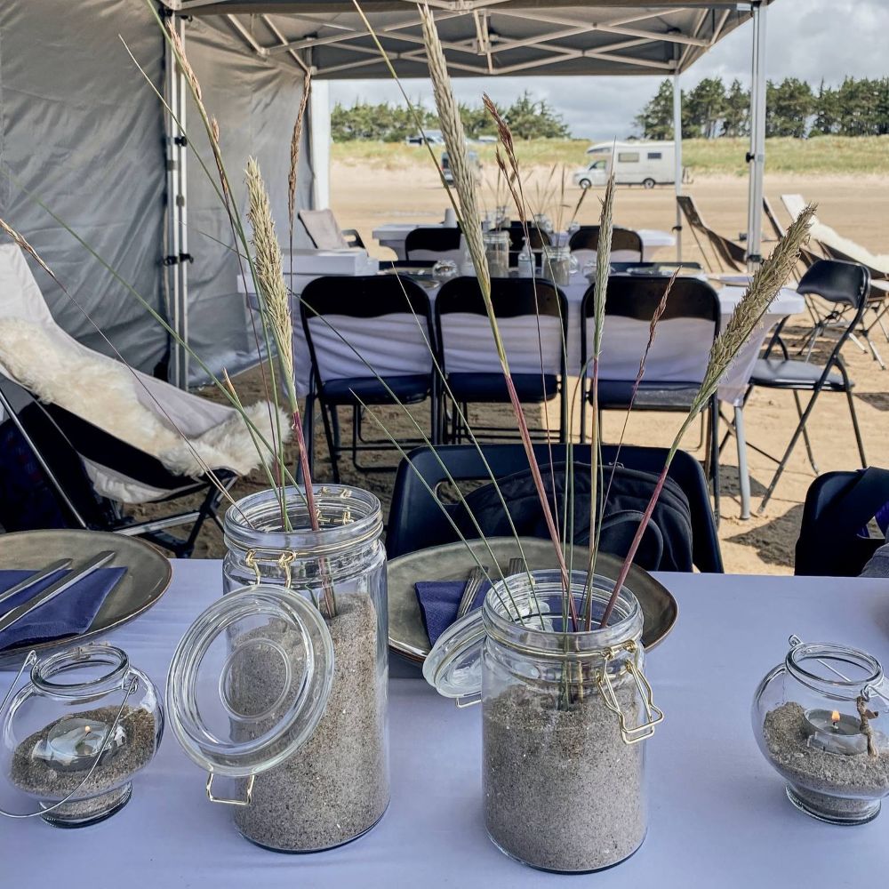 Bordopdækning til en hyggeligt frokost efter en aktivitet på stranden i forbindelse med et Outdoor Meeting/konference: vi sætter telt og stole op for jer i forbindelse med afvikling af jeres event, hvor I så kan afholde et møde samtidigt.