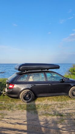 En sort bil med et sort tagtelt monteret og 2 cykler bagpå står parkeret med udsigt til havet
