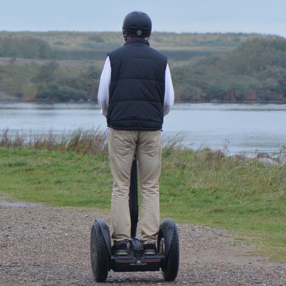 En mand set bagfra kører på Segway på en grussti. Book jeres næste event med os og oplev, hvordan et Segway Event kan løfte teamets samarbejde til nye højder!