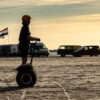 En ung kvinde kører på Segway på en strand, hvor solen er ved at gå ned. Book jeres næste event med os og oplev, hvordan et Segway Event kan løfte teamets samarbejde til nye højder!