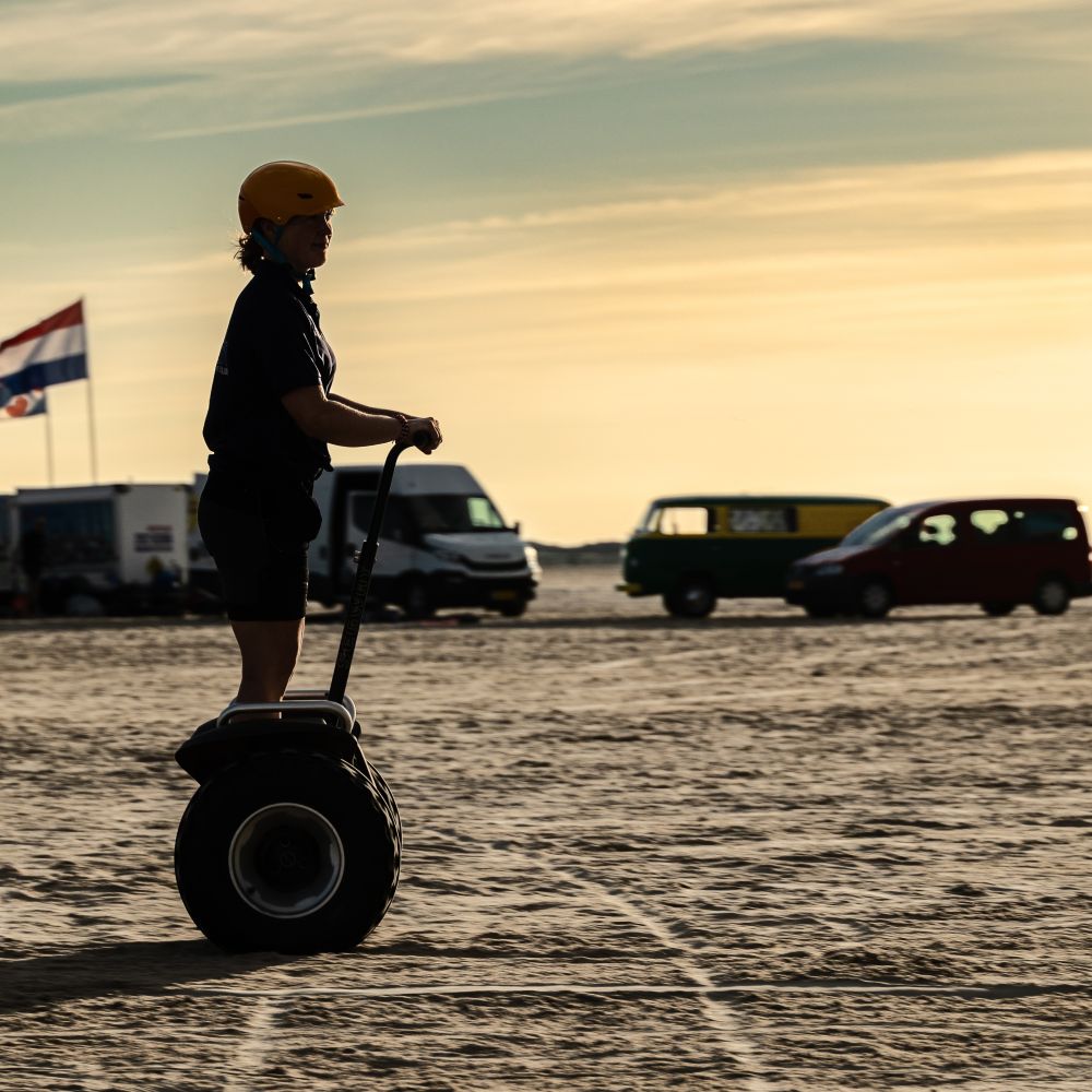 En ung kvinde kører på Segway på en strand, hvor solen er ved at gå ned. Book jeres næste event med os og oplev, hvordan et Segway Event kan løfte teamets samarbejde til nye højder!