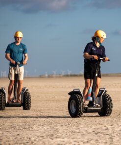 En ung kvinde og en ung mand kører på Segway på en strand, hvor solen skinner. Book jeres næste event med os og oplev, hvordan et Segway Event kan løfte teamets samarbejde til nye højder!