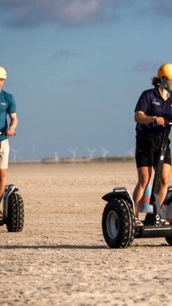 En ung kvinde og en ung mand kører på Segway på en strand, hvor solen skinner. Book jeres næste event med os og oplev, hvordan et Segway Event kan løfte teamets samarbejde til nye højder!