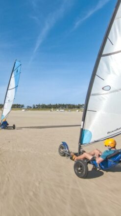 To strandsurfere kører på en flad, bred strand på Rømø på en dag med blå himmel.