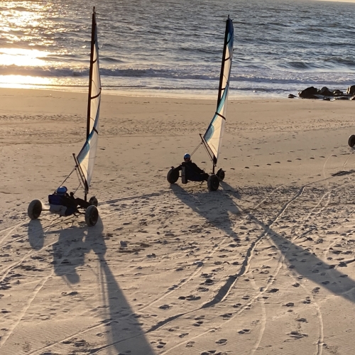 To strandsurfere kører på en strand med solnedgang i baggrunden