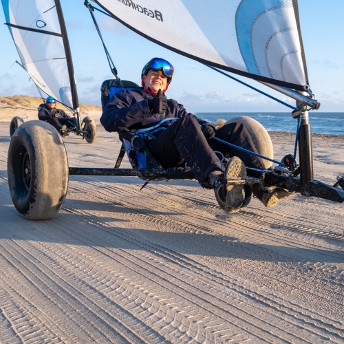 Nærbillede af en glad und mand i en strandsurfer på en flad sandstrand med blå himmel.