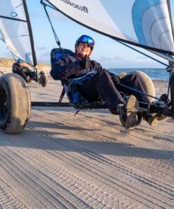 Smilende ung mand sidder i en strandsurfer på en bred strand med blå himmel i baggrunden