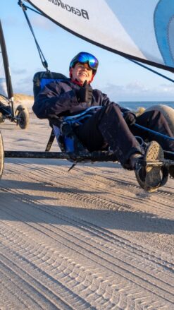 Smilende ung mand sidder i en strandsurfer på en bred strand med blå himmel i baggrunden