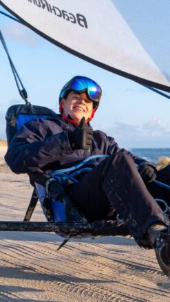 Smilende ung mand sidder i en strandsurfer på en bred strand med blå himmel i baggrunden