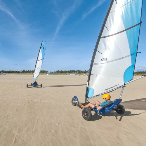 To strandsurfere kører på en flad, bred strand på Rømø på en dag med blå himmel.