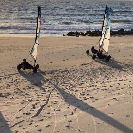 Tre strandsurfere kører på stranden med store sten og haven i baggrunden.