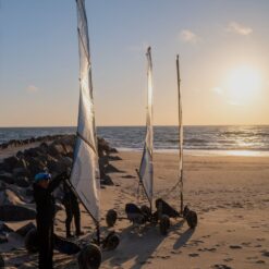 Tre strandsurfere står på en strand med solnedgangen i baggrunden.