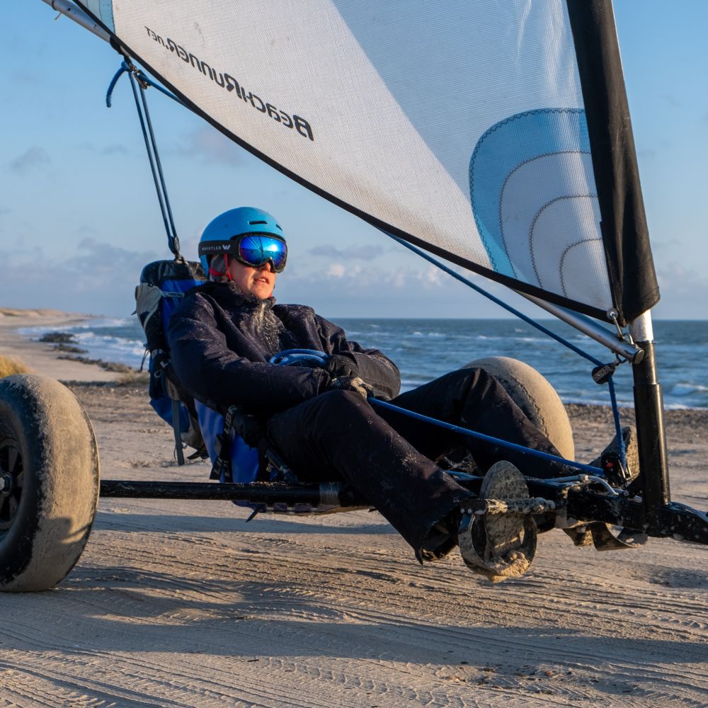 En ung mand kører i en strandsurfer. I hans skibriller spejler solen sig.
