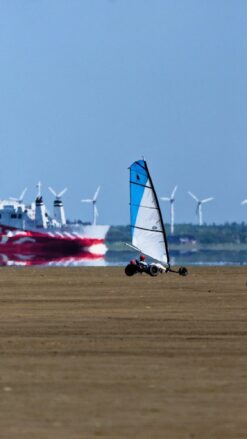 1 dobbelt og 1 single strandsurfer med hvidt og blåt sejl kører på en bred flad strand på Rømø- I baggrunden ses færgen til Sylt.