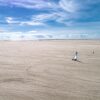 En enlig strandsurfer kører på en strand, der syner uendelig. Himlen er blå.