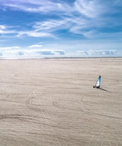 En enlig strandsurfer kører på en strand, der syner uendelig. Himlen er blå.