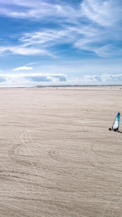 En enlig strandsurfer kører på en strand, der syner uendelig. Himlen er blå.