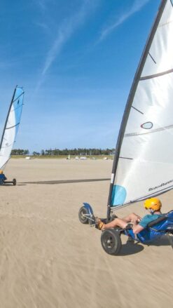 To single strandsurfere med hvidt og blåt sejl kører på en bred flad strand på Rømø