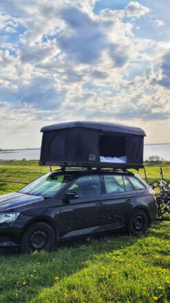 En sort bil med et sort tagtelt står på en græsplæne med kystlinje i baggrunden