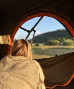 En ung kvinde med blond går ligger i et tagtelt og kigger ud på udsigten