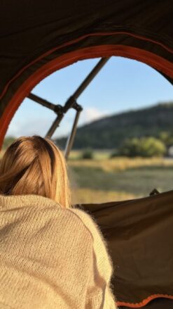 En ung kvinde med blond hår ligger i et tagtelt og kigger ud på udsigten