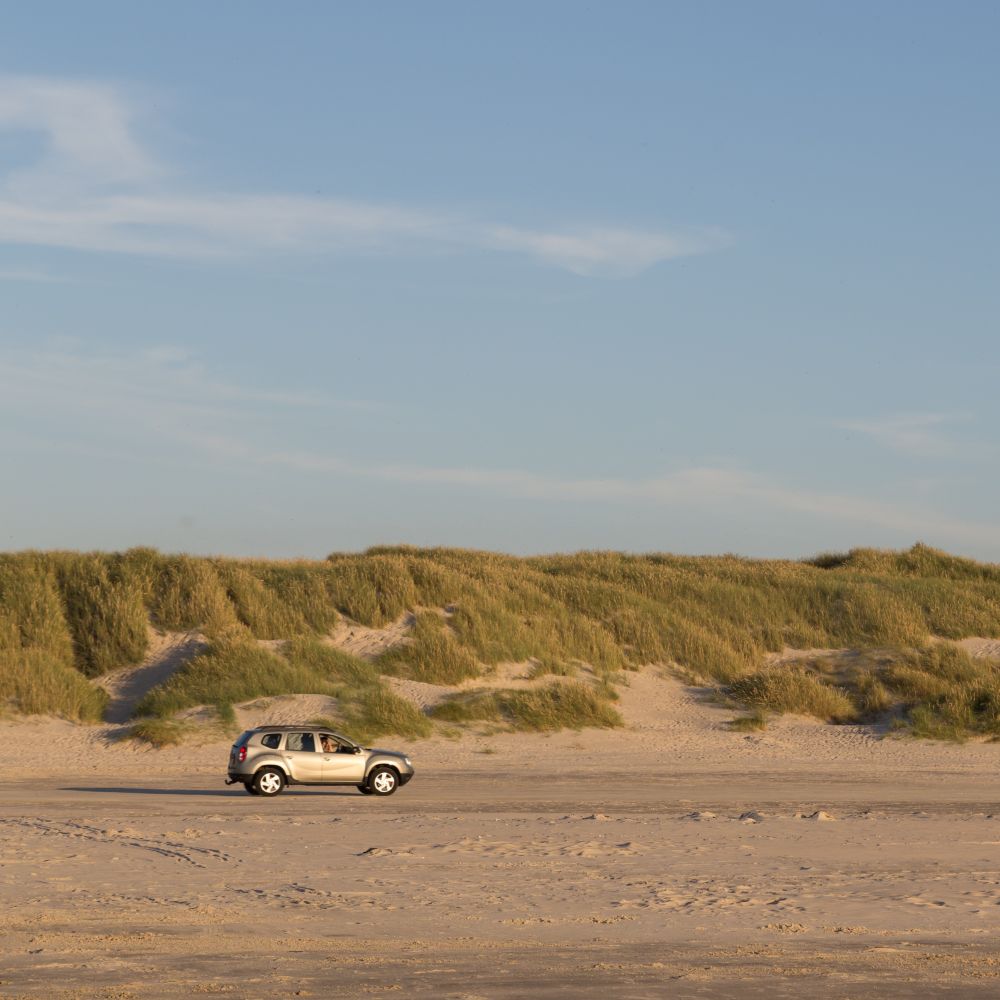 En sølvfarvet bil kører på stranden i Danmark